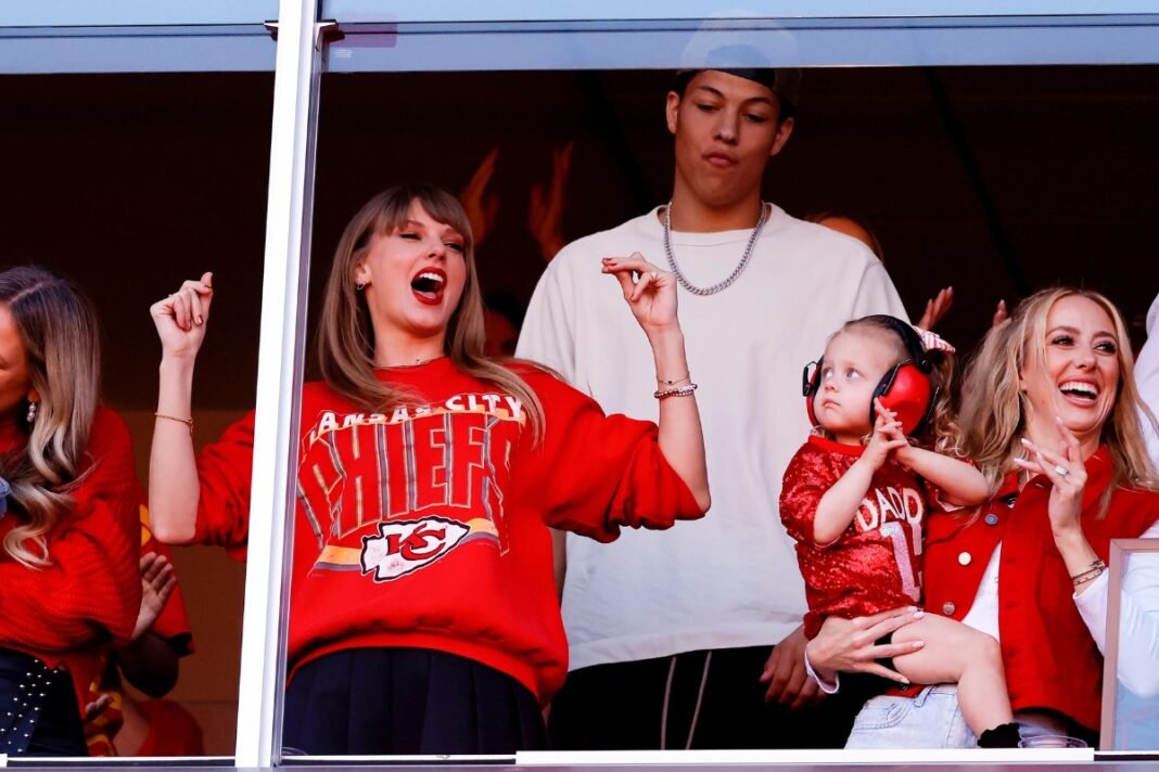 Taylor Swift cheers at Travis Kelce's Chiefs game wearing a red Kansas City team sweatshirt alongside Brittany Mahomes holding her baby