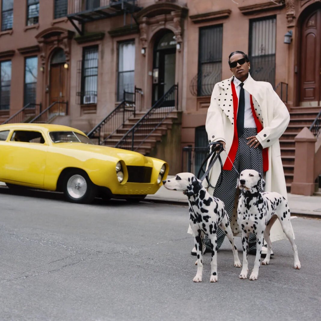 A$AP Rocky wearing a white polka dot coat with red accents and sunglasses, walking two Dalmatian dogs on a Harlem street with brownstone buildings and a yellow vintage car in the background.