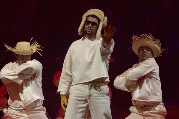 Bad Bunny center stage in white ensemble with straw hat, flanked by dancers in traditional Puerto Rican jíbaro attire during his historic Coliseo residency performance, July 2025