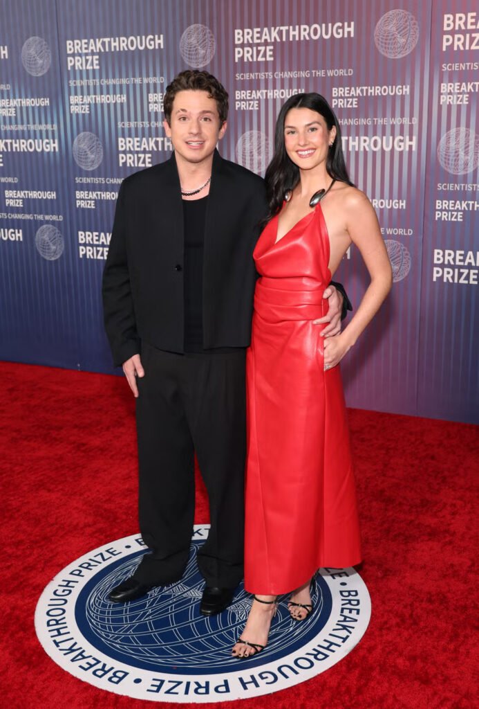 Charlie Puth and Brooke Sansone attend the Breakthrough Prize ceremony on red carpet, with Puth in black suit and Sansone in red halter gown