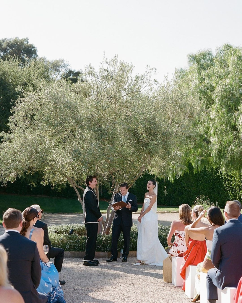 Charlie Puth and Brooke Sansone outdoor wedding ceremony with guests seated under olive trees in garden setting