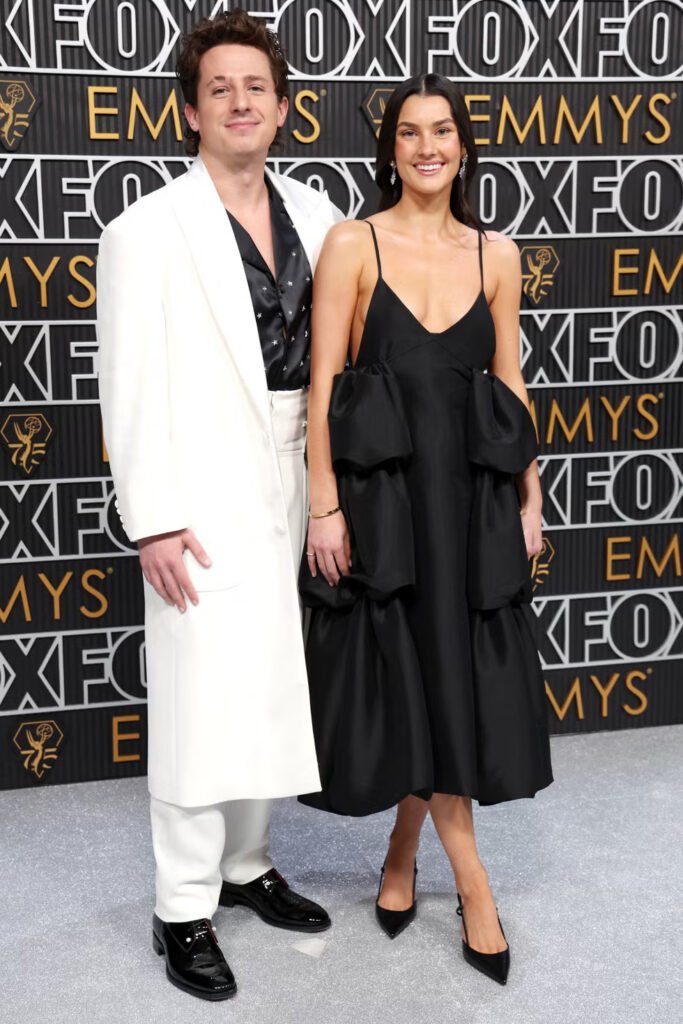 Charlie Puth and Brooke Sansone pose at Emmy Awards event, Puth wearing white blazer and Sansone in black sculptural dress