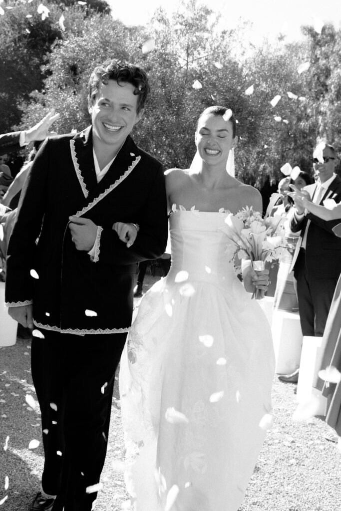 Charlie Puth and Brooke Sansone walk down aisle as newlyweds with flower petals falling, black and white wedding photo