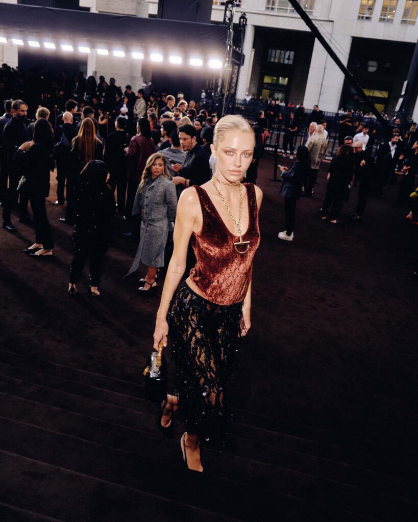 Delilah Belle walking through crowd at Gucci Spring 2026 presentation wearing burgundy sequined top and black lace skirt