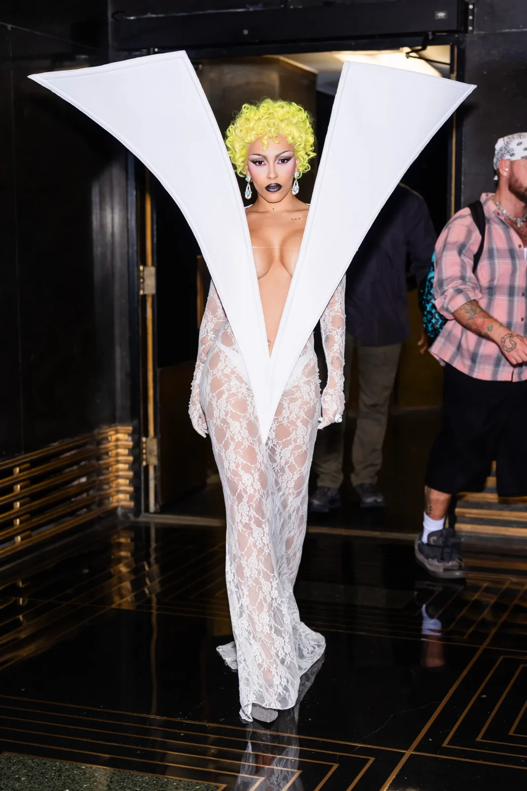 Doja Cat wearing the iconic Quine Li white lace gown with dramatic oversized sculptural lapels and bright yellow curly wig at Saturday Night Live