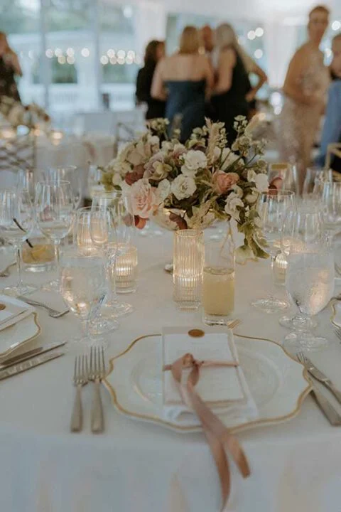Elegant wedding reception table setting with blush rose centerpiece, gold-rimmed china and candlelight