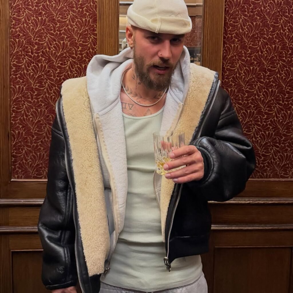 Justin Bieber poses with champagne in classic hotel setting wearing layered shearling and leather jacket