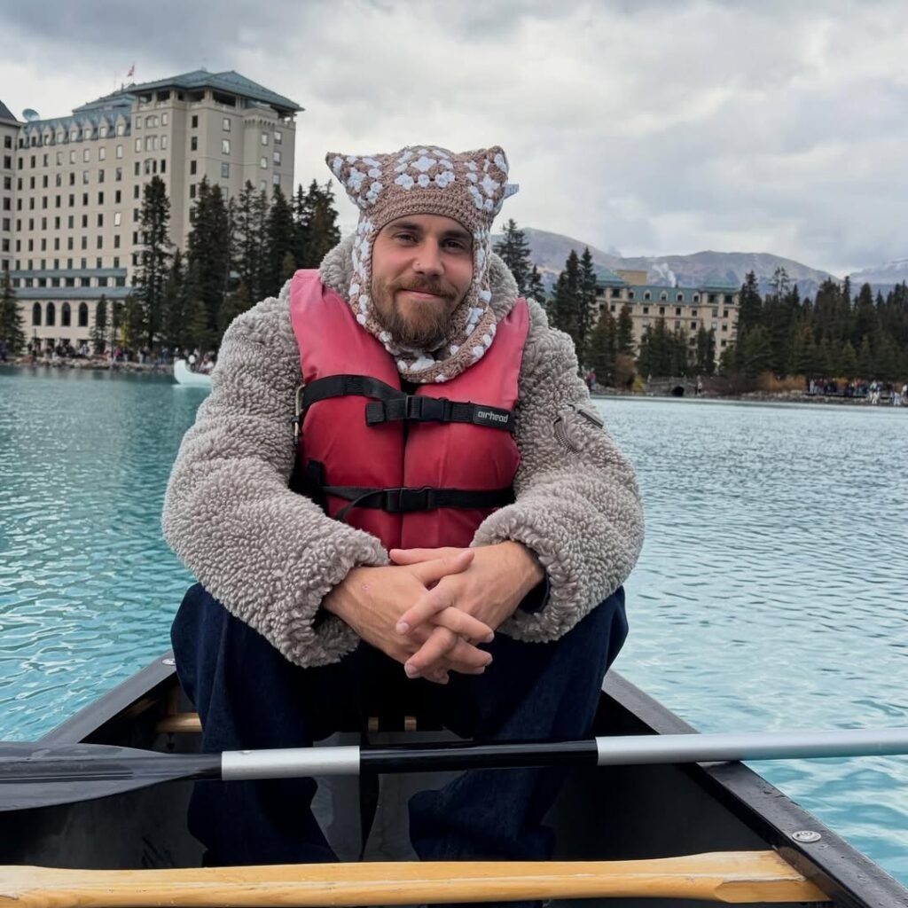 Justin Bieber sits in canoe wearing life jacket and knit beanie on turquoise mountain lake at luxury resort