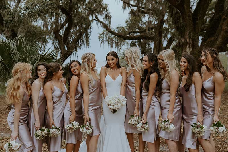 Marissa Lawrence with bridesmaids in champagne satin dresses holding white bouquets under moss-draped oak trees