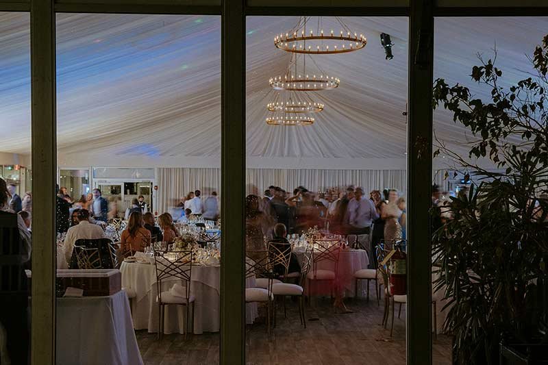 Tented wedding reception with circular chandelier and guests dining at elegantly decorated tables