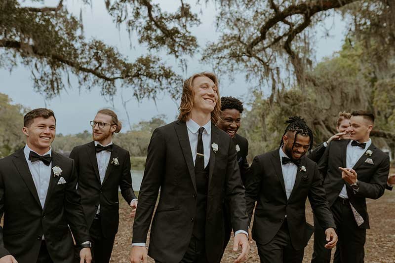 Trevor Lawrence with groomsmen in black tuxedos and bow ties laughing together at wedding ceremony