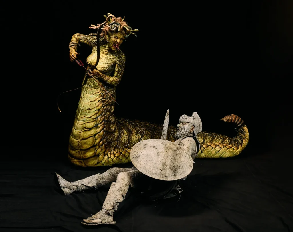 Heidi Klum posing in complete Medusa costume with serpent tail and stone warrior prop at Halloween event