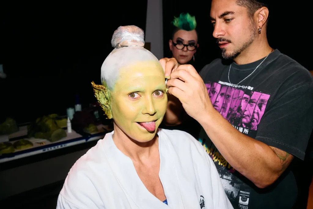 Makeup artist applying prosthetics to Heidi Klum showing custom split tongue during Medusa transformation.