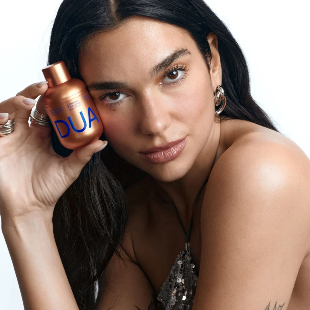 Model with glowing skin holding DUA Skincare serum in bronze bottle, showcasing radiant complexion results from accessible luxury skincare