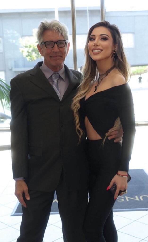 Lika O with Eric Roberts in elegant black cutout outfit posing with the Academy Award nominated actor in formal suit at professional venue