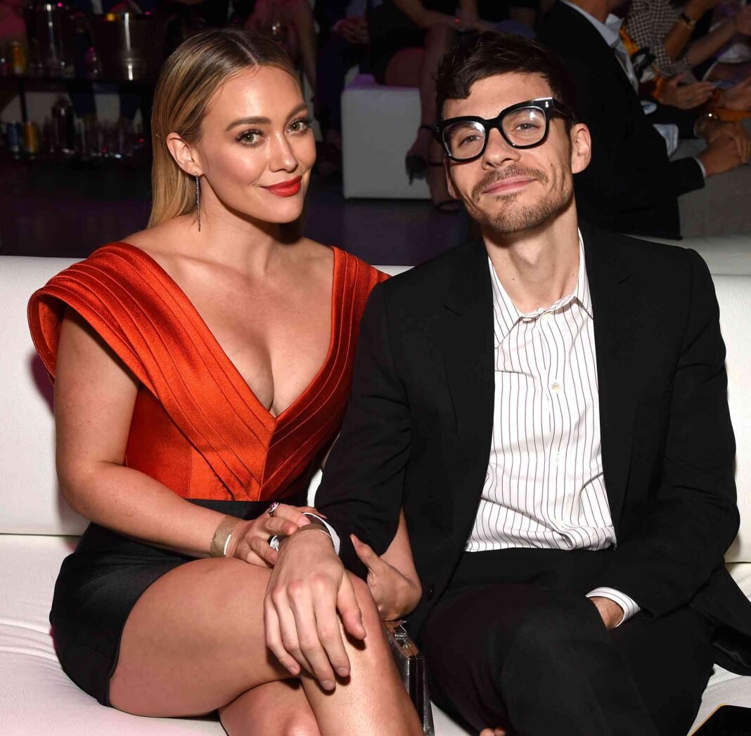 Hilary Duff and Matthew Koma attend an entertainment industry event, with Duff wearing a red dress and Koma in a black suit with striped shirt and glasses