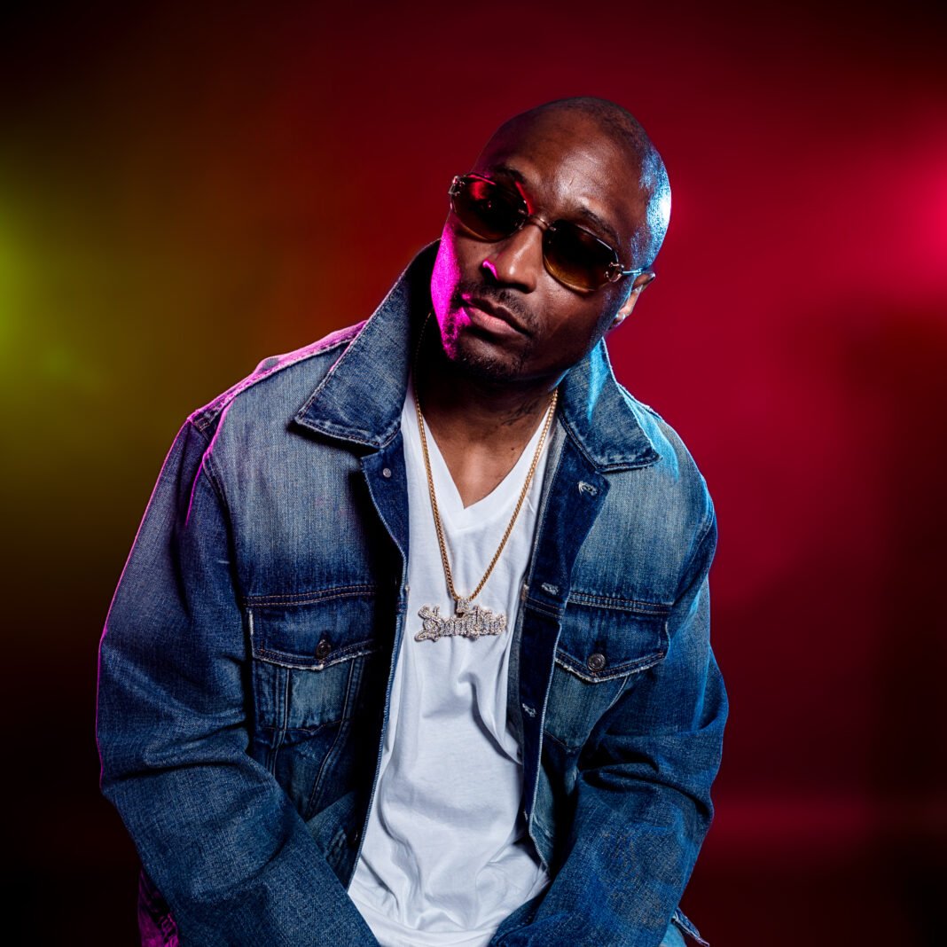 Hip-hop artist Don Che in denim jacket and sunglasses against colorful gradient background