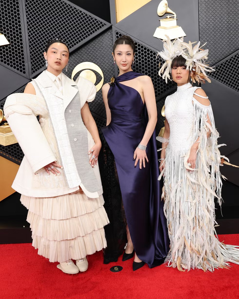 Audrey Nuna, Rei Ami, and another artist pose together at the 2026 Grammy Awards wearing custom designer ensembles that celebrate their cultural heritage and personal identity
