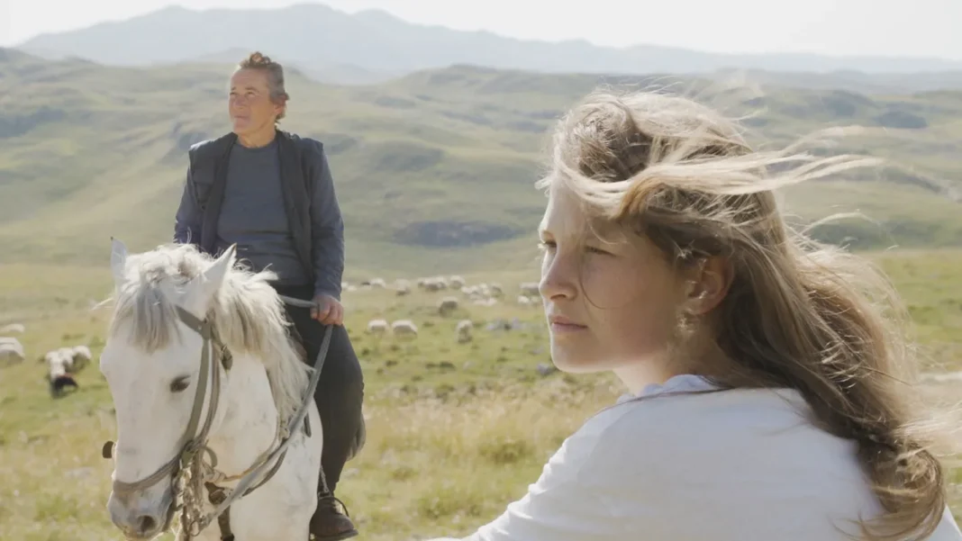 Woman on white horse and young girl in windswept mountain landscape from To Hold a Mountain movie