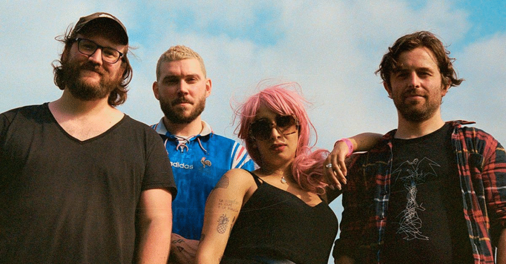 Mandy Indiana band members Valentine Caulfield with pink hair and three male bandmates photographed outdoors against blue sky in casual attire