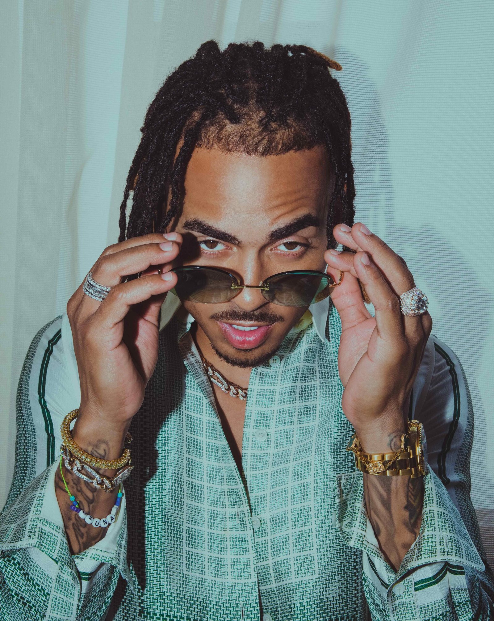 Ozuna peers over rimless tinted sunglasses wearing a green plaid shirt and layered diamond and gold jewelry in a Flaunt Magazine cover shoot