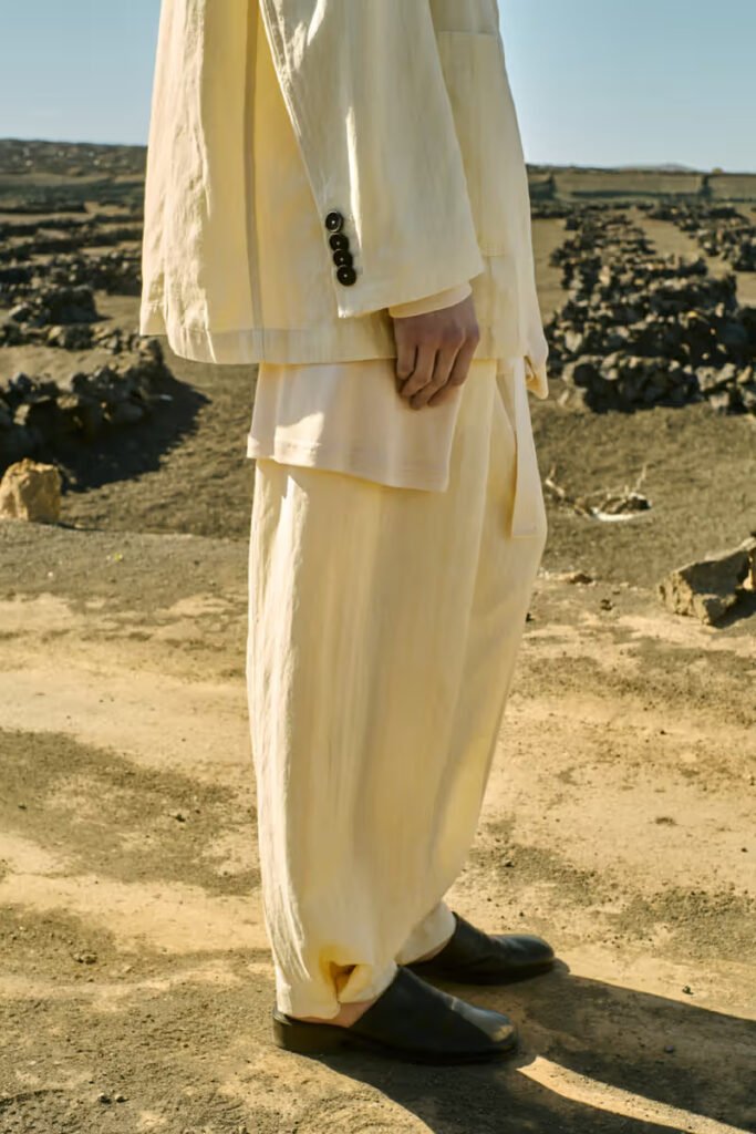 Side-view-detail-of-an-ivory-linen-suit-with-voluminous-trousers-and-black-loafers-set-against-an-arid-volcanic-landscape