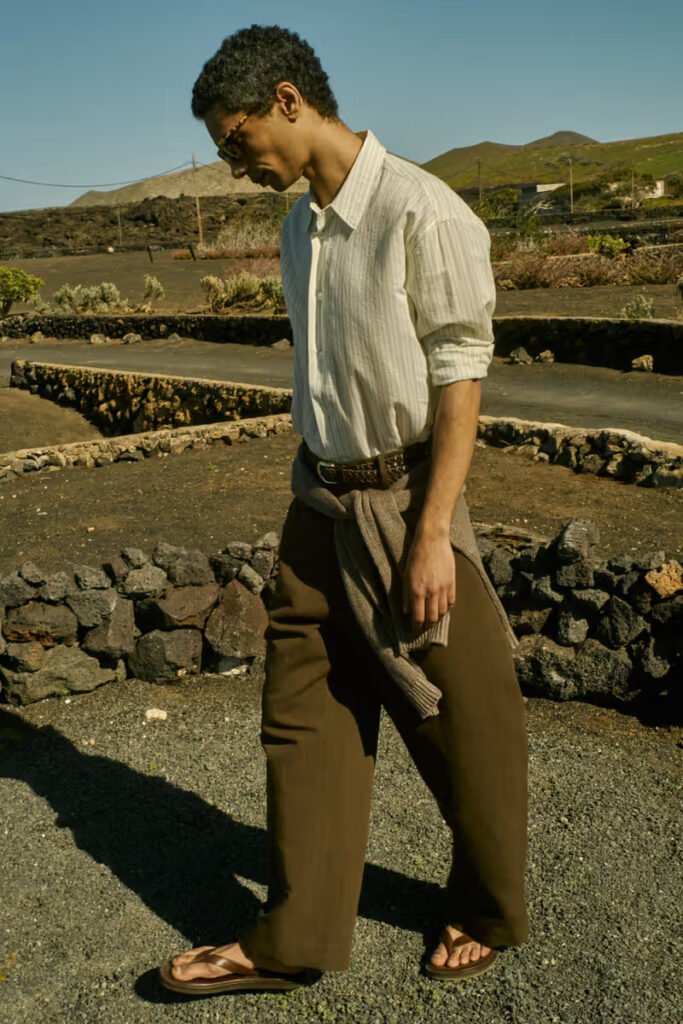 Studio-Nicholson-SS26-male-model-in-a-striped-linen-shirt-and-wide-leg-brown-trousers-walking-outdoors-on-location