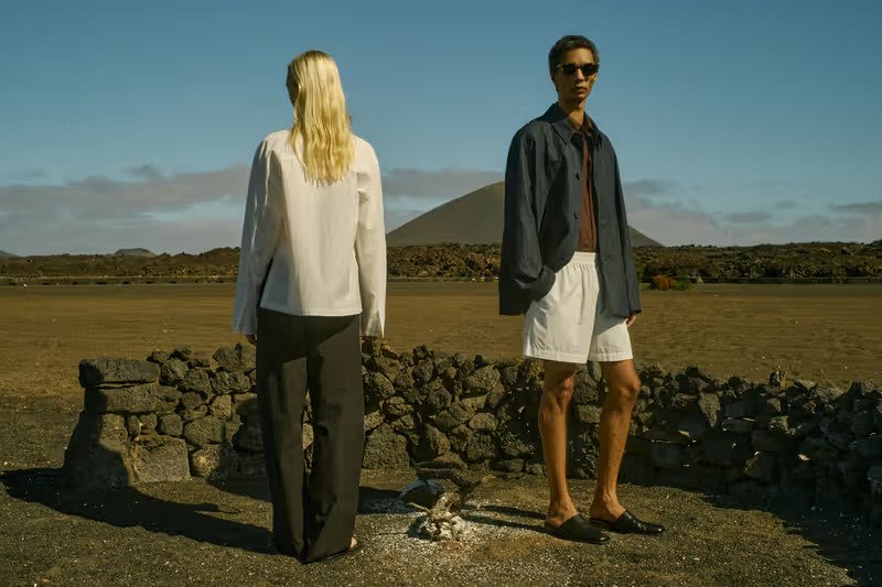 Studio-Nicholson-SS26-two-models-in-relaxed-separates-standing-beside-a-volcanic-stone-wall-against-an-open-landscape