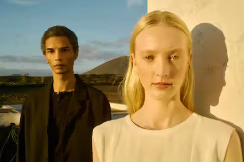 Two models in minimalist outfits — cream top and black blazer — photographed against a volcanic landscape in golden hour light.