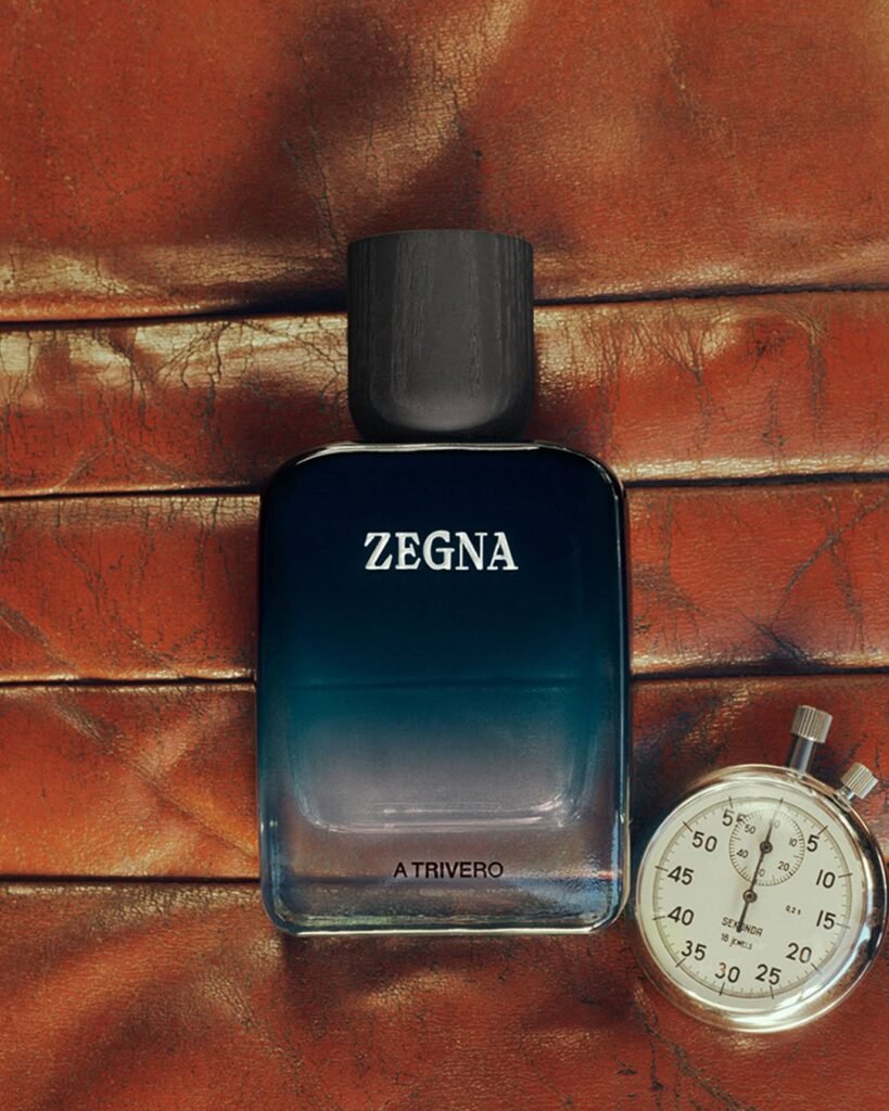 ZEGNA-MEMORIE-A-Trivero-fragrance-bottle-in-deep-teal-gradient-laid-flat-on-aged-red-leather-alongside-a-vintage-silver-stopwatch