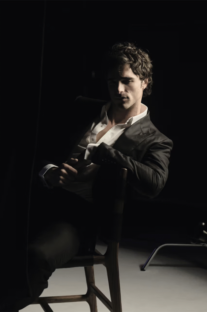 Jacob-Elordi-Bleu-De-Chanel-2026-campaign-dark-studio-portrait-in-open-collar-suit-holding-fragrance-bottle
