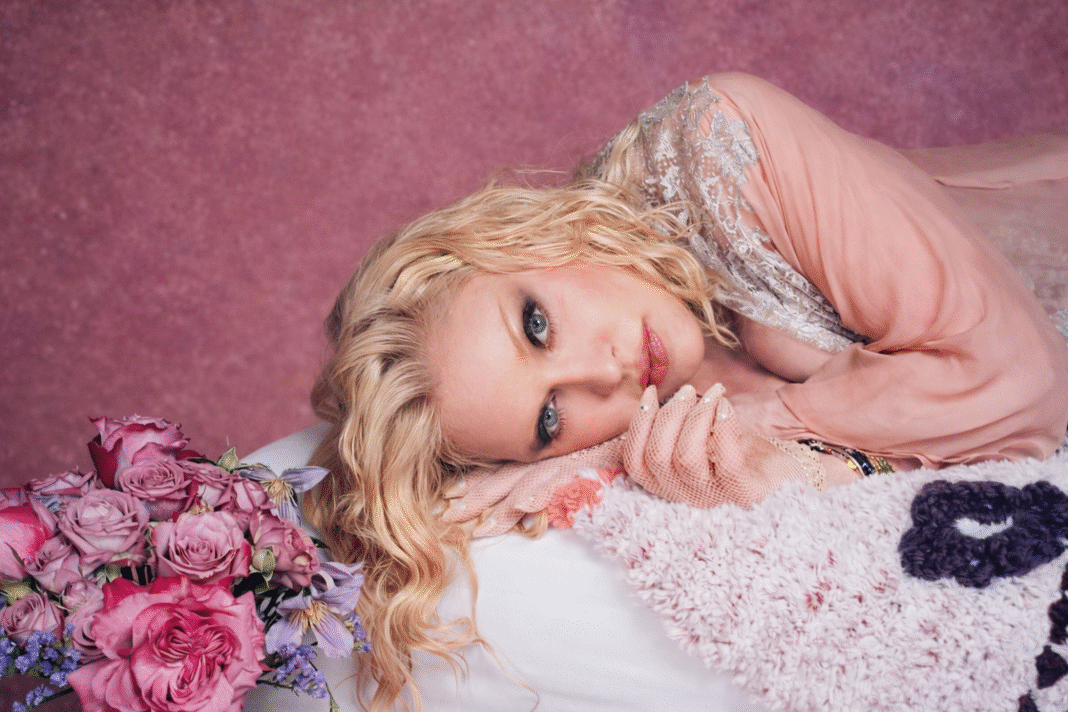 Madonna lying on a pink blanket beside a bouquet of roses, looking at the camera