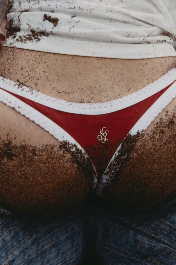 Close-up-of-a-red-bikini-bottom-with-white-contrast-trim-and-Nude-Project-monogram-logo-dusted-with-sand-from-the-SS26-Airplane-Mode-swimwear-collection