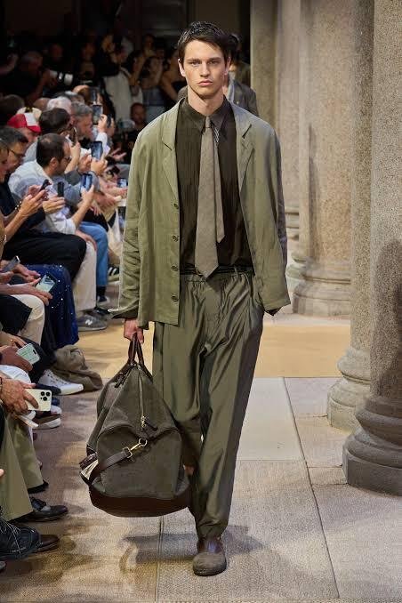 A-model-walks-the-Giorgio-Armani-SS27-menswear-runway-in-an-olive-jacket-and-trousers-with-a-contrasting-tie-carrying-a-duffel-bag
