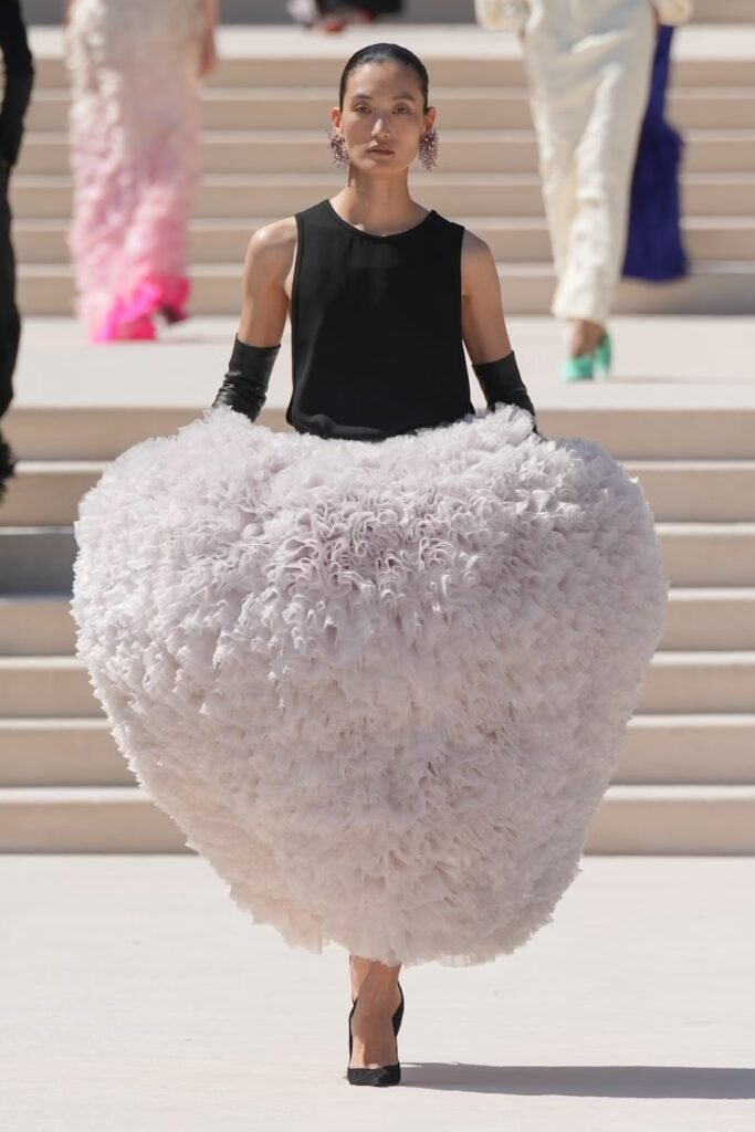 Model in a black sleeveless top and voluminous pale-pink ruffled tulle skirt with black leather gloves on the Balenciaga 55th couture runway in Paris.