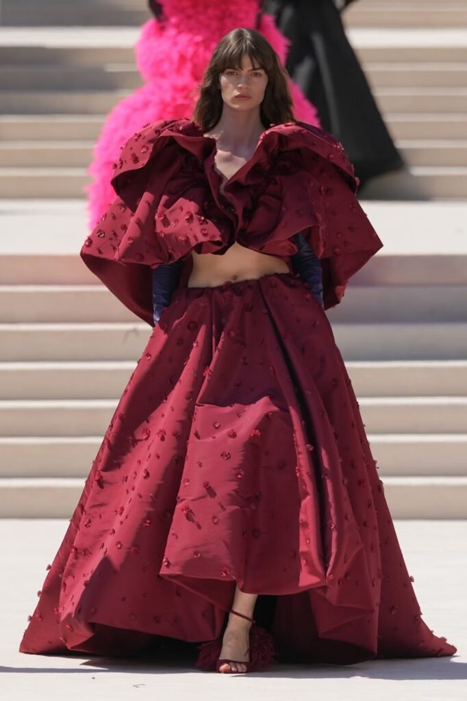 Model in a burgundy floral-appliqué cropped cape jacket and full ball skirt with feather-trimmed sandals on the Balenciaga 55th couture runway in Paris.