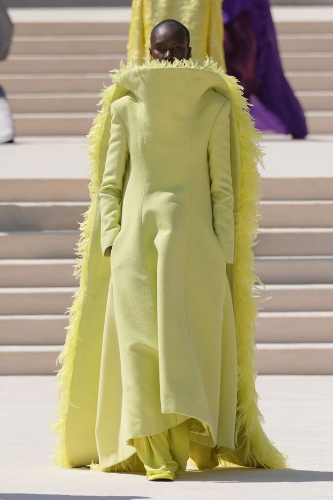 Model-in-a-chartreuse-floor-length-coat-with-a-high-funnel-collar-and-feather-trimmed-cape-on-the-Balenciaga-55th-couture-runway-in-Paris