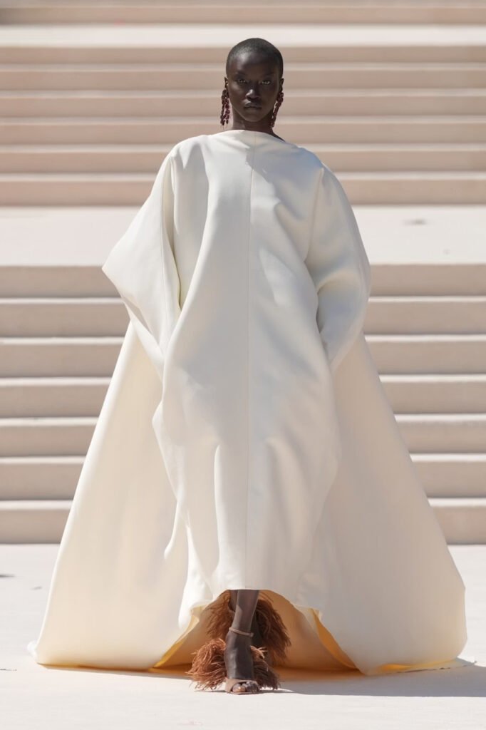 Model in a voluminous ivory cocoon-shaped gown with brown feather-trimmed sandals on the Balenciaga 55th couture runway in Paris.