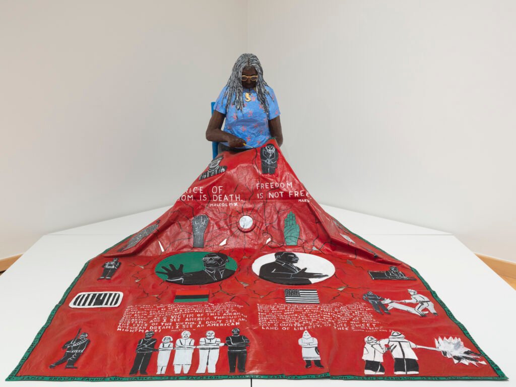 Willie Birch sculpture of a woman sewing a red quilt honoring Malcolm X and MLK, at CAAM's Stories to Tell