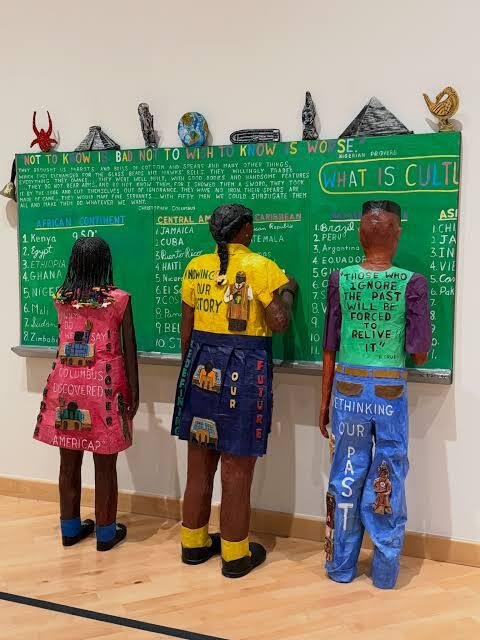 Willie-Birch-sculpture-of-three-children-writing-at-a-green-chalkboard-in-Stories-to-Tell-at-CAAM