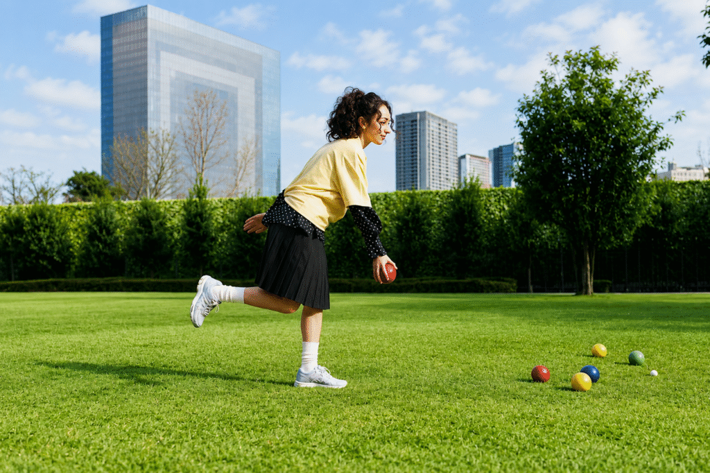 Woman-in-a-yellow-top-pleated-skirt-and-white-sneakers-bowls-on-a-city-lawn-ASICS-Sensory-Bloom-editorial-look