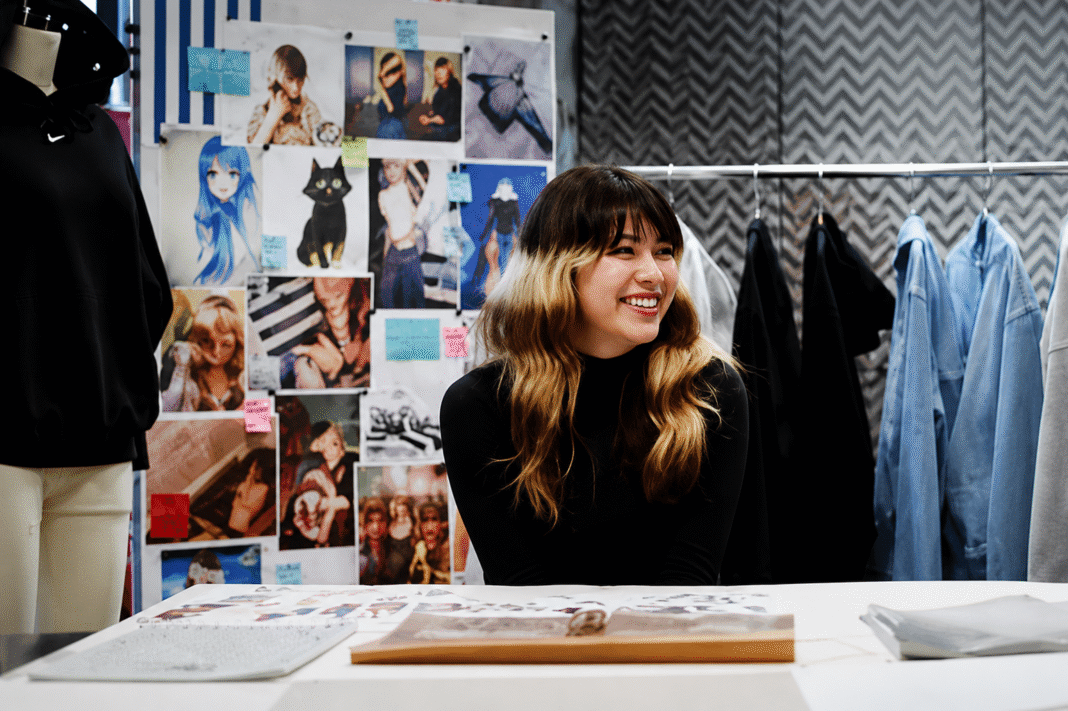 Alysa Liu smiling at a studio workspace in front of a mood board of sketches and fabric swatches for the Nike Studio Fleece campaign