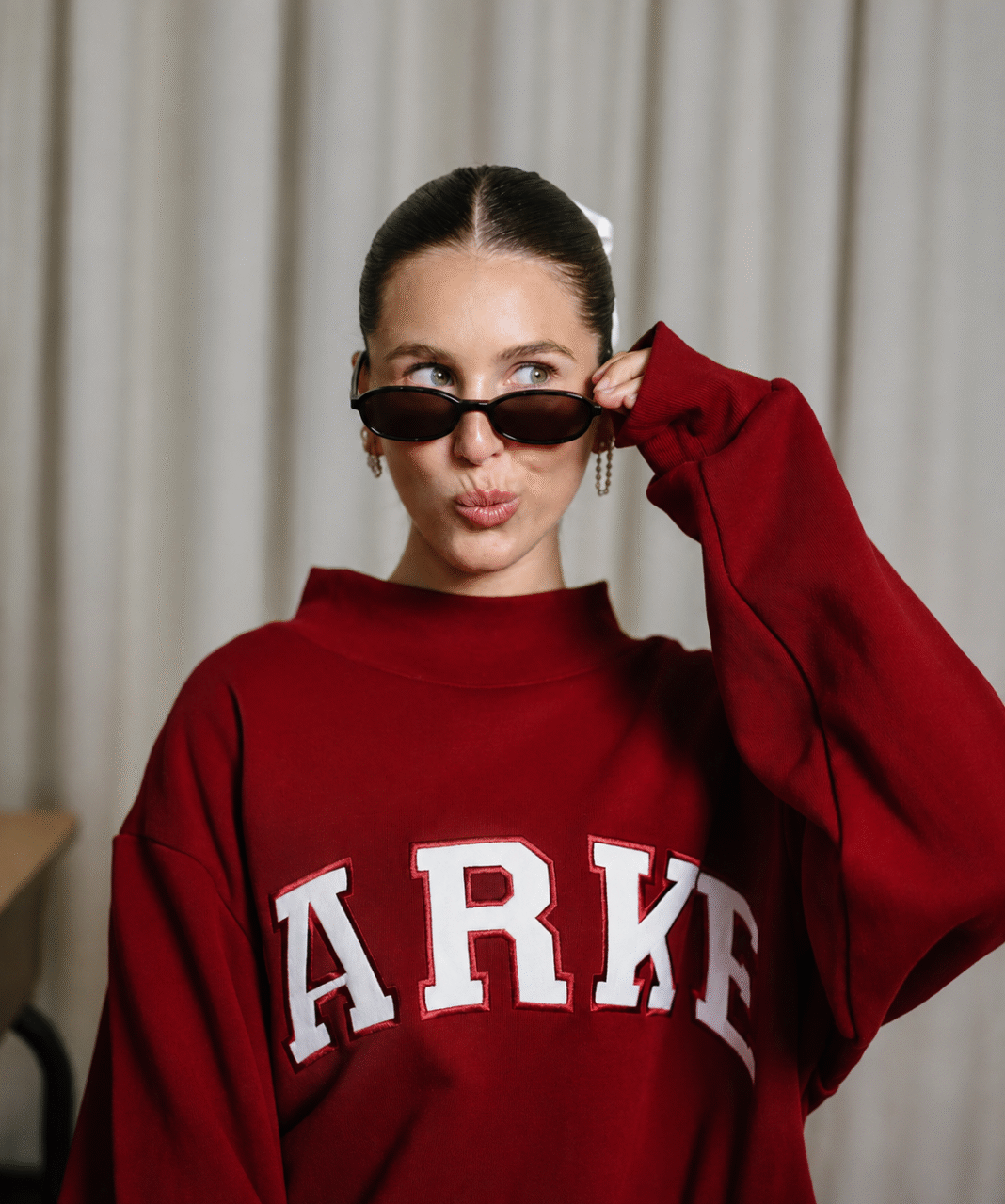 Chelsea Parke Goles wears a burgundy Parke sweatshirt while posing with sunglasse