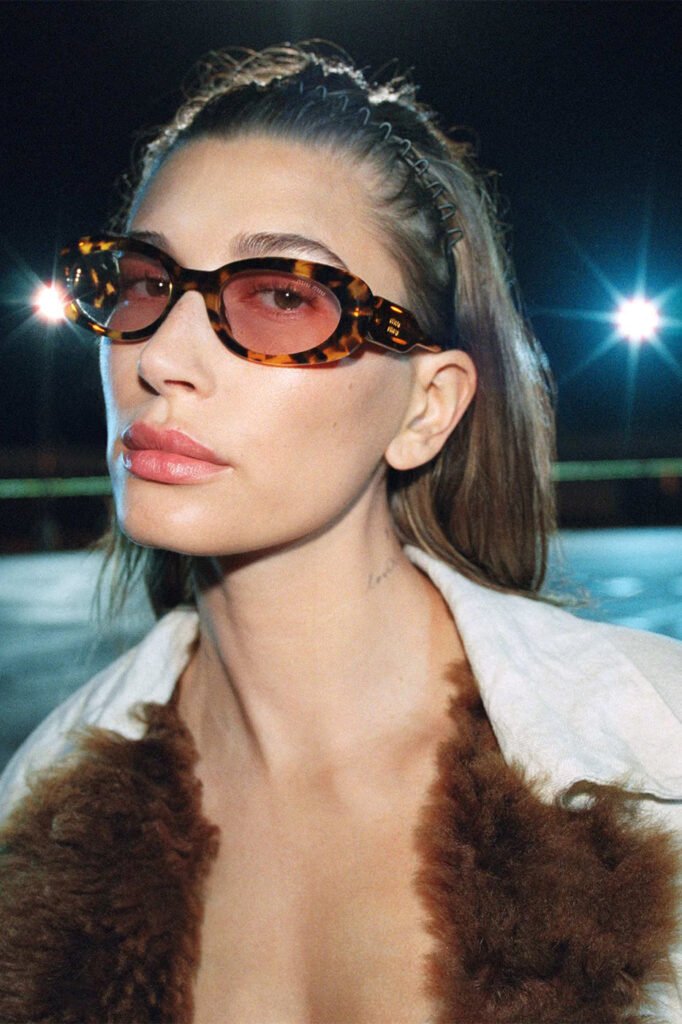 Hailey-Bieber-in-tortoiseshell-red-tinted-Miu-Miu-sunglasses-and-a-fur-trimmed-coat-photographed-at-night-for-the-Miu-Miu-FallWinter-2026-campaign