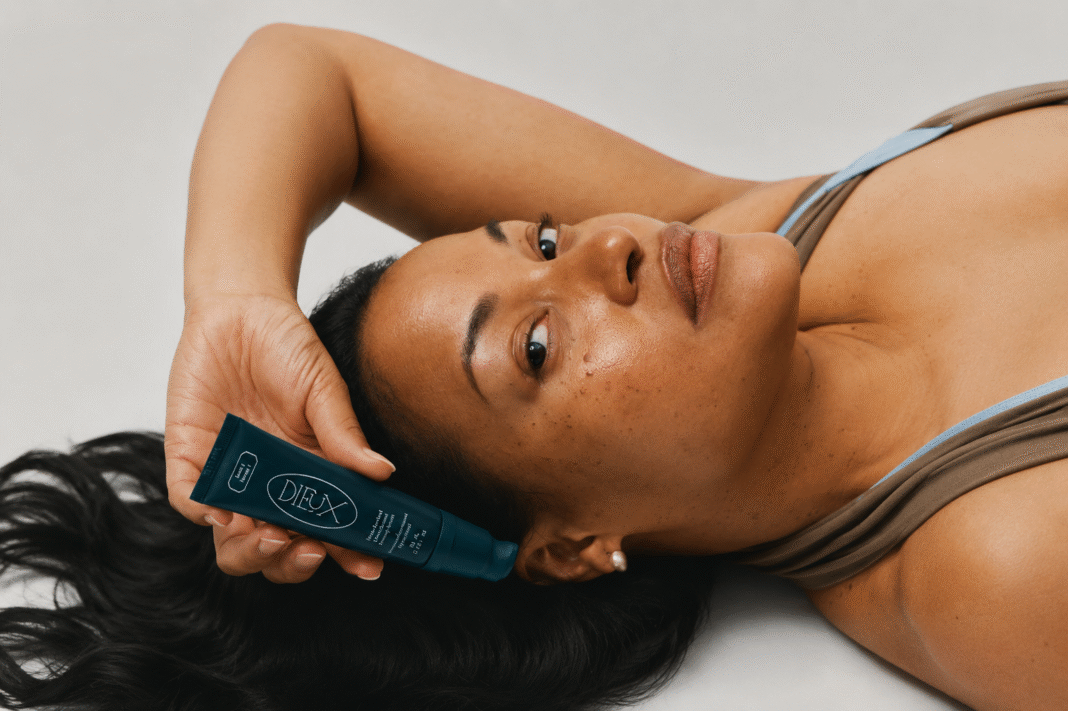 Model holds Dieux Firm Revival retinal serum in teal tube against dewy, radiant skin