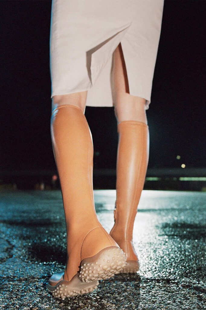 Tan-knee-high-Miu-Miu-boots-with-studded-soles-worn-under-a-cream-skirt-photographed-at-night-for-the-Miu-Miu-FallWinter-2026-campaign