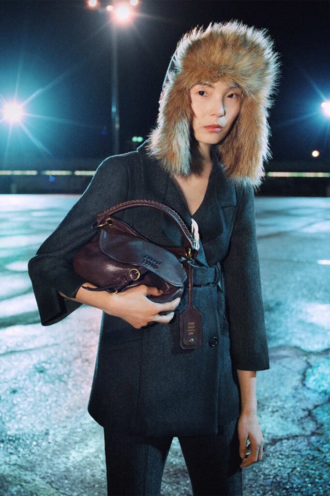 Xiao-Wen-Ju-in-a-fur-trapper-hat-and-grey-coat-holding-a-burgundy-leather-Miu-Miu-bag-photographed-at-night-for-the-Miu-Miu-FallWinter-2026-campaign