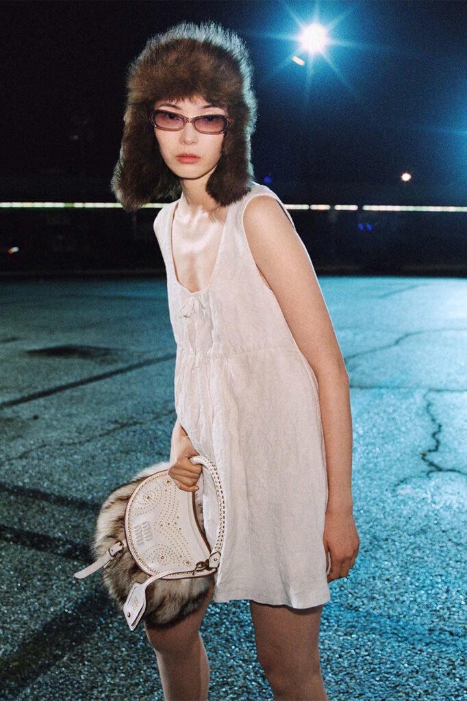 Xiao-Wen-Ju-in-a-fur-trapper-hat-tinted-sunglasses-and-a-white-slip-dress-holding-a-studded-white-Miu-Miu-bag-photographed-at-night-for-the-Miu-Miu-FallWinter-2026-campaign.