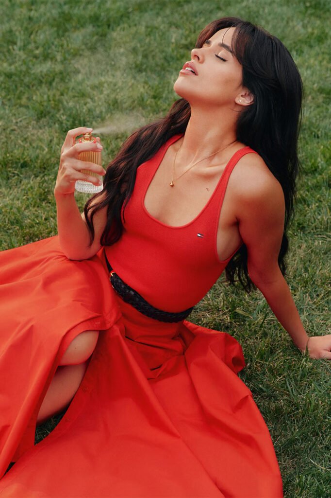 Camila-Cabello-sits-on-the-grass-in-a-red-Tommy-Hilfiger-dress-eyes-closed-spritzing-Freedom-Eau-de-Parfum