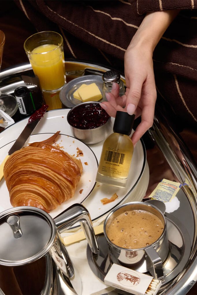 Hand-reaching-for-a-DedCool-Mocha-Magic-bottle-on-a-room-service-tray-with-a-croissant-jam-and-espresso